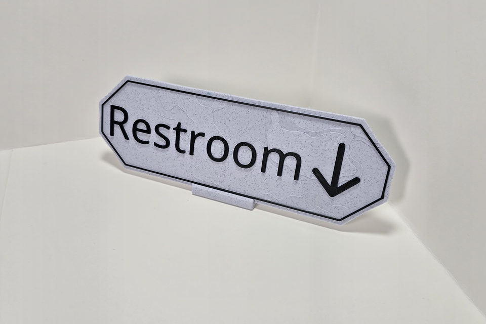 Marble White and Matte Black angled destination sign reading Restroom with a down arrow on a Marble White tabletop stand.