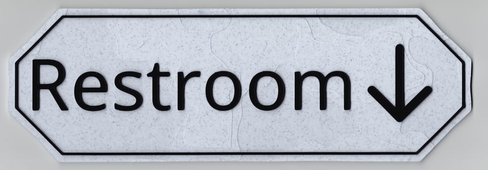 Direct scan of a Marble White Restroom sign with matte black wording, border, down arrow, and angled corners.