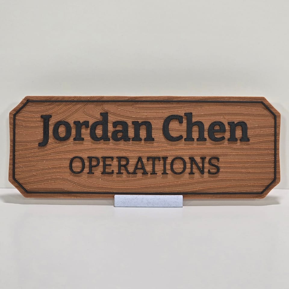 Wood-look office nameplate reading Jordan Chen and Operations on a marble-white tabletop stand.