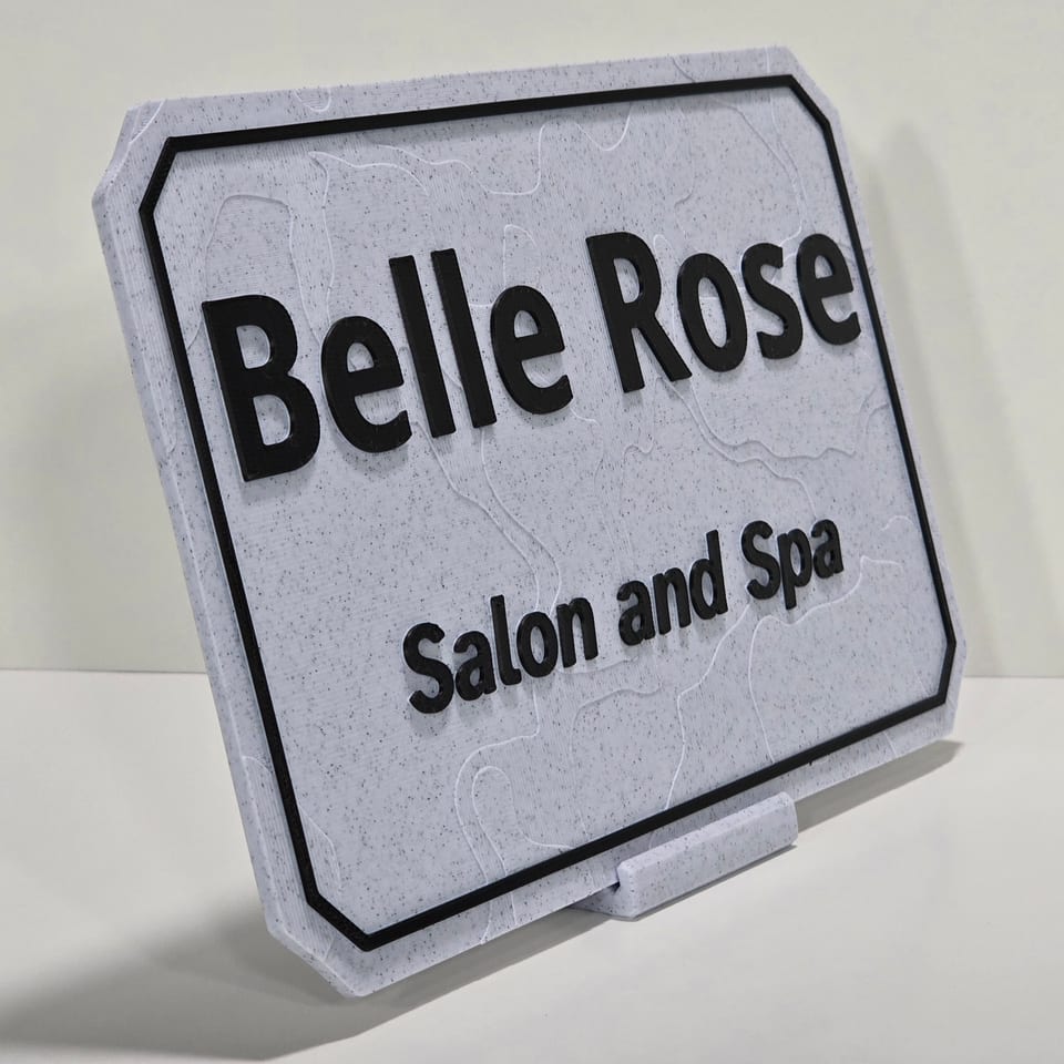 Angled marble-white business plaque reading Belle Rose and Salon and Spa on a matching tabletop stand.
