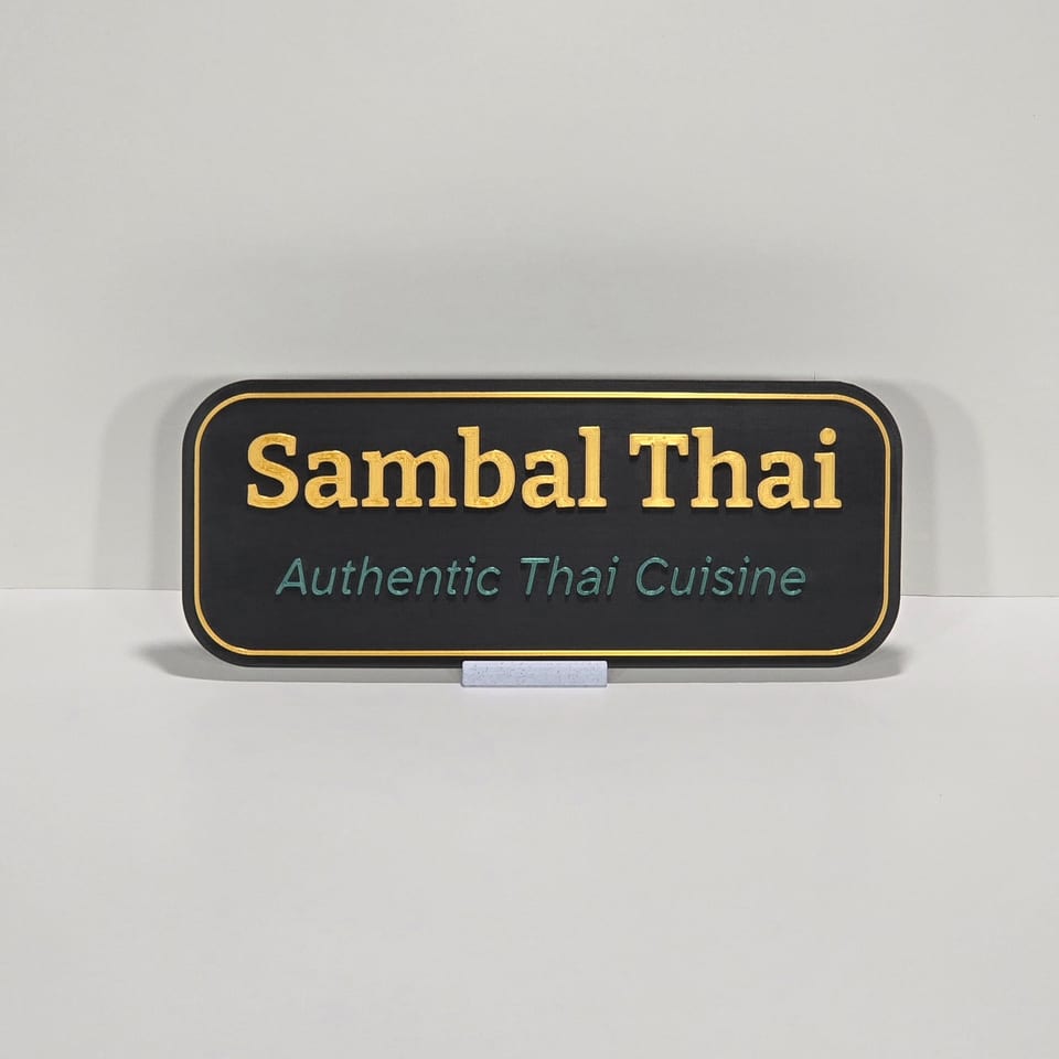 Black business plaque reading Sambal Thai and Authentic Thai Cuisine on a marble-white tabletop stand.