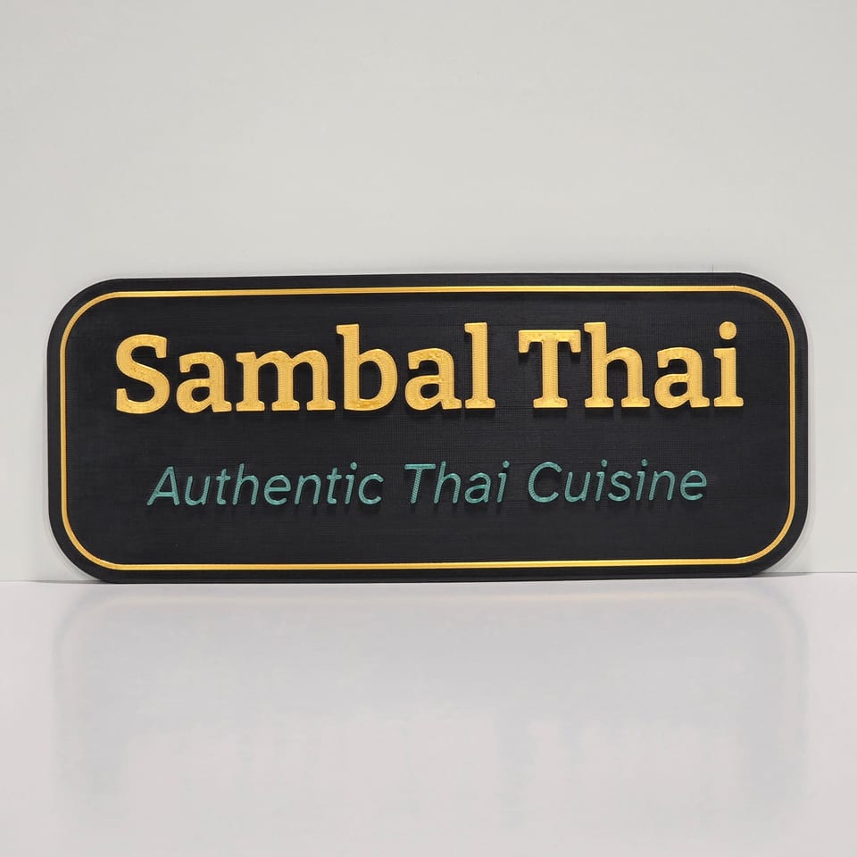 Straight-on black business plaque reading Sambal Thai and Authentic Thai Cuisine with gold and green lettering and a gold border.