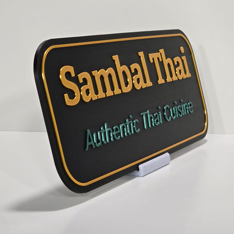 Angled black business plaque reading Sambal Thai and Authentic Thai Cuisine on a marble-white tabletop stand.