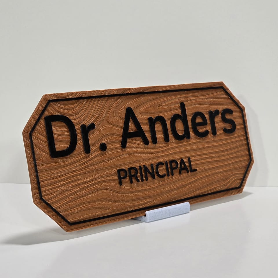Angled wood-look staff nameplate reading Dr. Anders and Principal on a marble-white tabletop stand.