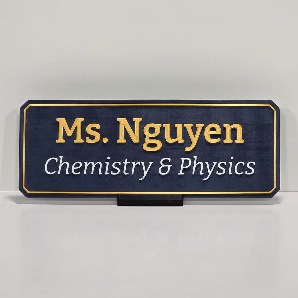 Navy teacher nameplate reading Ms. Nguyen and Chemistry & Physics on a black tabletop stand.