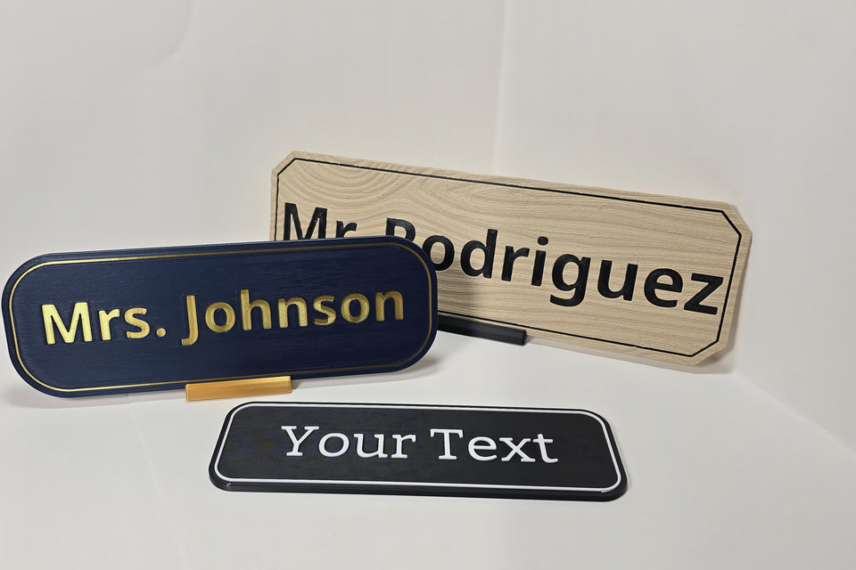 Higher-angle view of three Teacher and Staff Desk Nameplate samples arranged on a white tabletop backdrop.